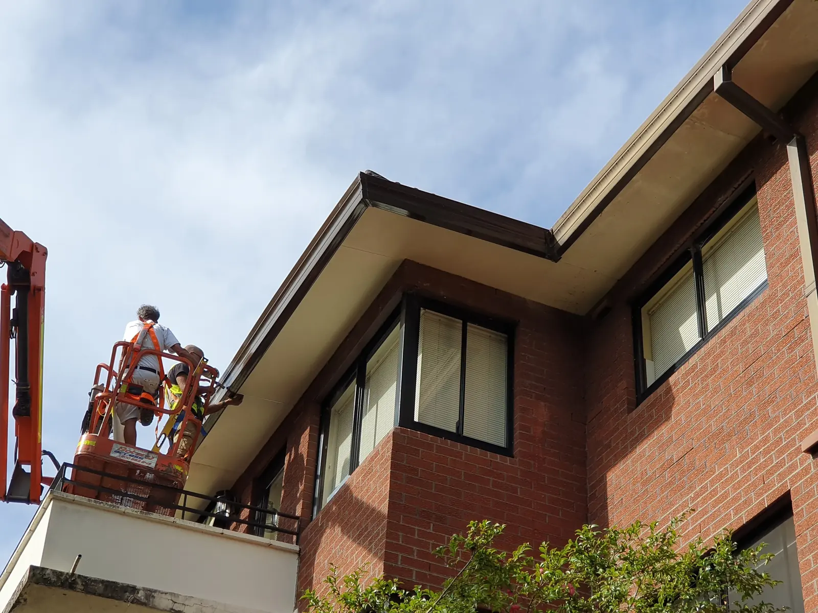 Worker in a knuckle-boom platform beside the eaves of the Lane Cove brick apartment building