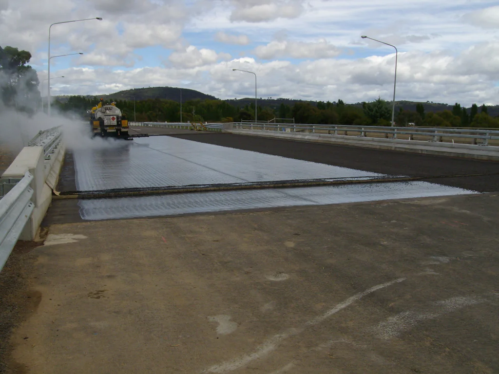 Road surfacing truck applying binder to a bridge deck